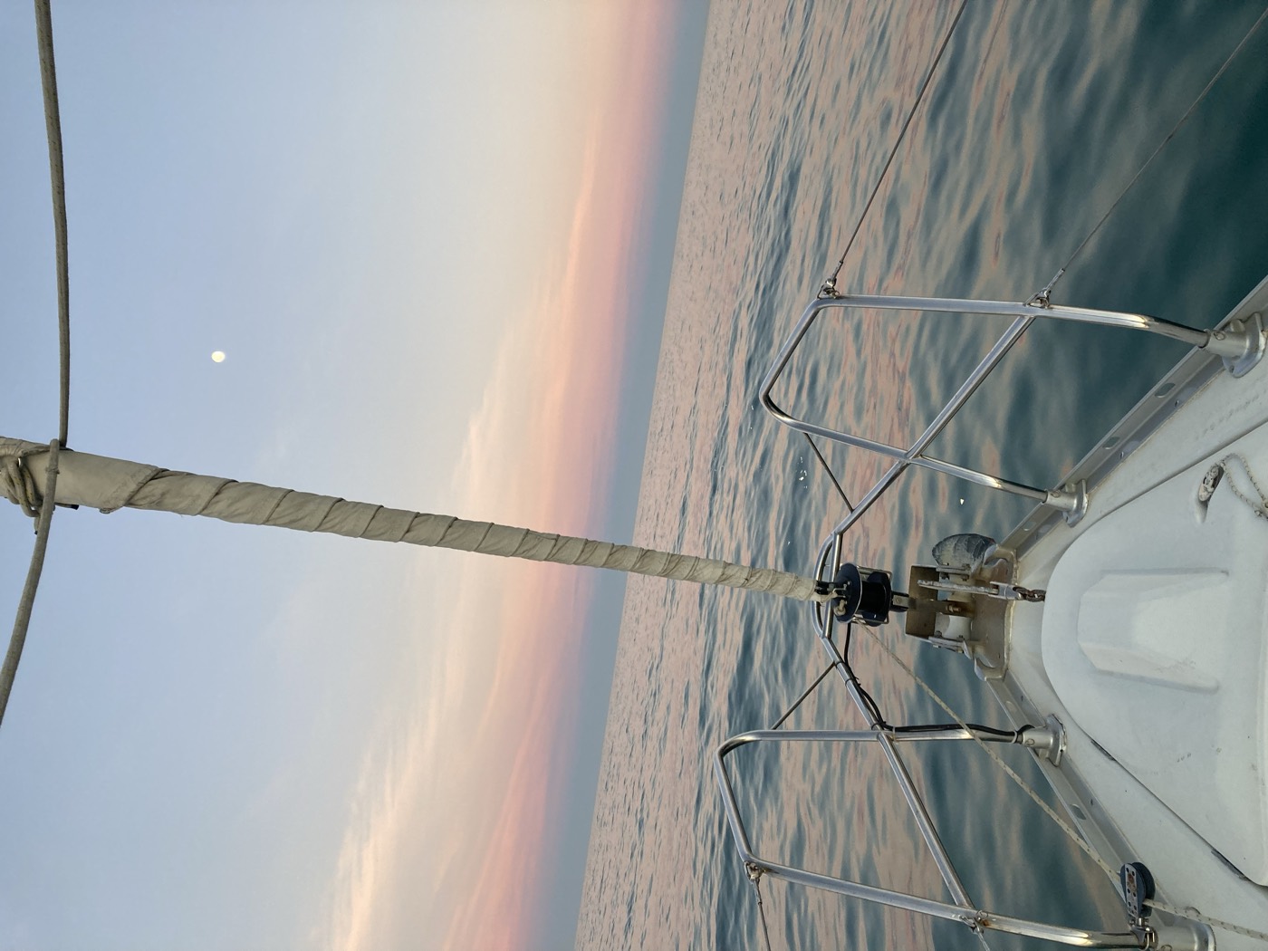 the bow of a sailing boat on still water under a pink dusk sky with the moon up