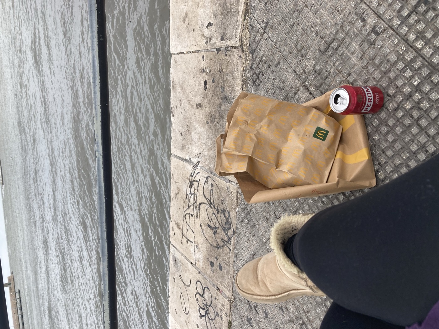 a fast food bag and a can of peroni on a harbour edge by the sea